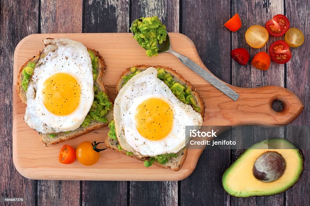 Avocado, egg open sandwiches on paddle board Avocado, egg open sandwiches on whole grain bread with tomatoes on paddle board with rustic wood table Avocado Stock Photo