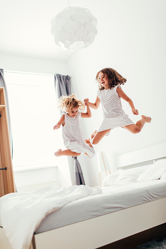 Sisters having fun in daddy's and mommy's bedroom. Jumping and holding hands together. The younger one is 4 years old and the older on is 8 years old. Shot with Canon EOS 5Ds and 35/1.4L  50 Mpx image.