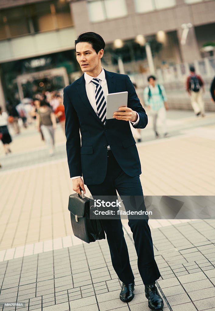 Mixed ethnicity businessman using tablet Young mixed ethnicity businessman is using a tablet outside during he walk. He is walking quickly on the city street and seems like he searching for something. 2015 Stock Photo