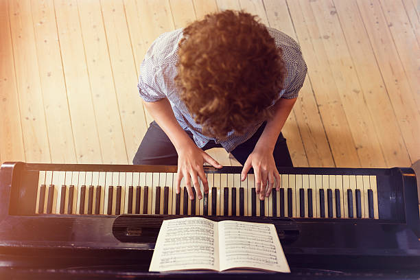 blickwinkel von teenager-jungen spielen klavier im sonnenlicht zimmer - piano keyboard instrument one person piano key stock-fotos und bilder