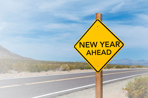 New Year Ahead road sign with blue cloudy sky and blur background.