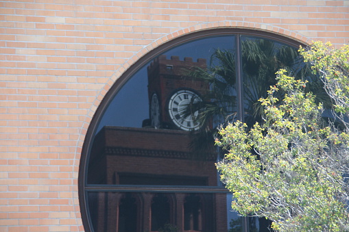 The clock tower of the First Congregational Church is reflected in the unique round window of the First United Methodist Church in Redlands, CA.