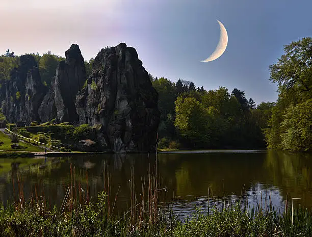 The bright moon hovers over a rock formation.
