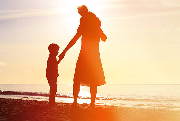 istock mother and two kids walking on beach at sunset 484712330