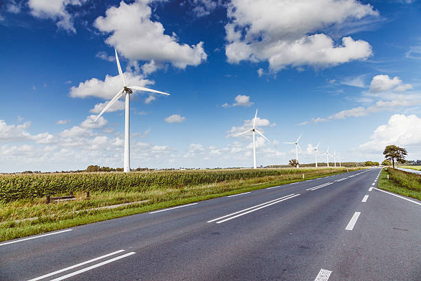 An empty dutch's country road and a row of wind turbines in a corn field.  Summer cloudy and windy day in Holland