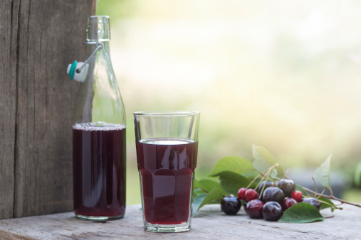 Homemade cherry juice on a rustic background decorated with cherries and leaves.