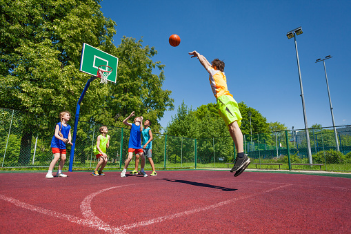 Boy performs foul shot at basketball game on the playground during sunny summer day