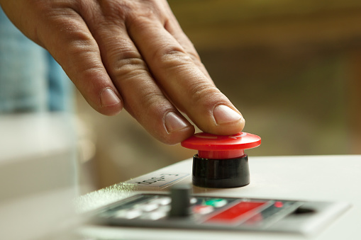 Male hand pushing emergency red stop button.