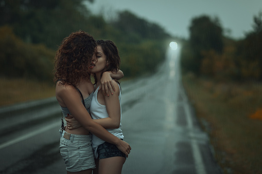 Girls lesbians kissing under the heavy rain.