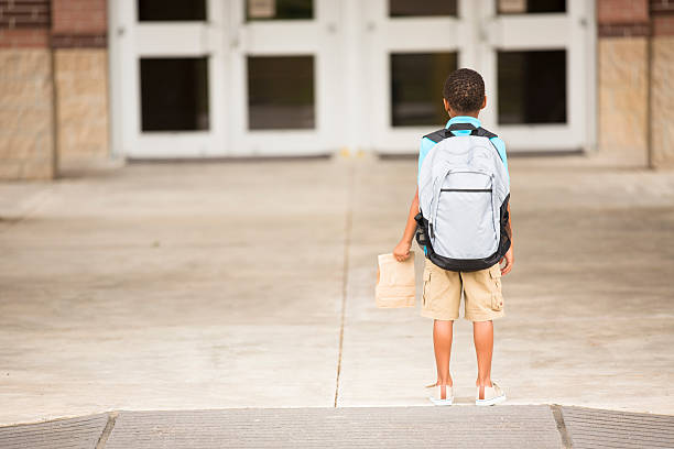 istock African descent, little boy faces school building. Lunch, backpack. 484725288
