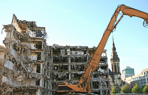 A demolished apartment house. An excavator standing in the background.