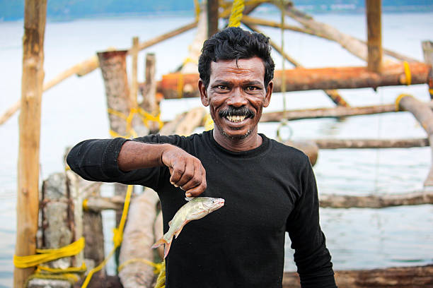 Smiling Fisherman Fishing at Fort Kochi Kerala India Kochi, India - April 21, 2009: Smiling fisherman holds up a small fish, with a so called Chinese fishing net equipment in the background, near Fort Kochi, Kerala, India. These fishing nets were introduced by Portuguese Casado settlers from Macau. cochin kerala india chinese fishing net stock pictures, royalty-free photos & images