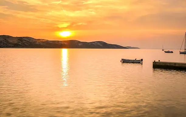 Peaceful sunset or sunrise by the sea with boats and sailship. Landscape od small harbour village at dusk or dawn. Vacation, leisure and relaxation on the sea side.