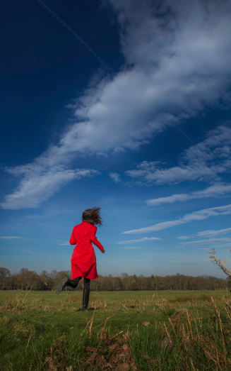 A young woman in a red coat runs across a meadow