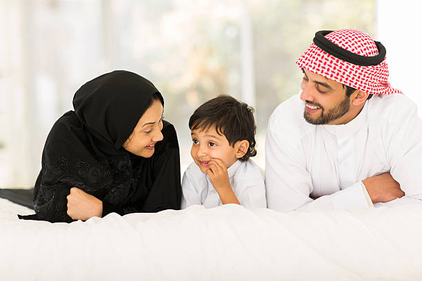 young muslim family lying on bed happy young muslim family of three lying on bed at home pics of a cute muslim outfits stock pictures, royalty-free photos & images