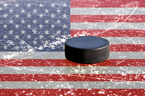 Black hockey puck on ice rink with flag of the United States