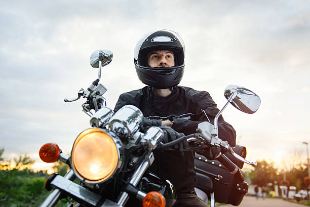 Biker in helmet driving motorcycle on sunset. Biker in helmet driving chopper motorcycle on sunset. Road in the city. Front view over the sky. biker stock pictures, royalty-free photos & images