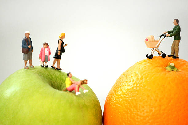 Frome, Somerset, England, UK - 10, April 2014: Concept image depicting a healthy eating theme, with a family of mini people (made by Bachmann Scenecraft models), shown walking along fresh fruit, of an orange and an apple.