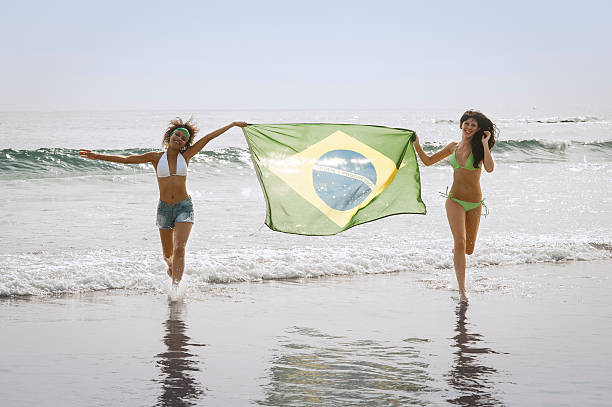 young beautiful girls running through surf with Brazil Flag stock photo