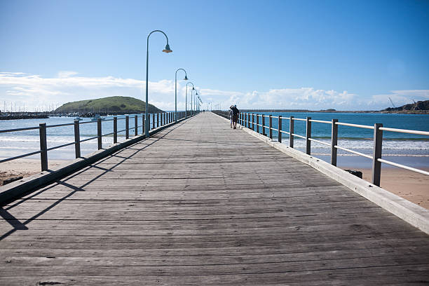 Coffs harbour pier, Australia. Coffs Harbour, Australia - March 22, 2014: Coffs Harbour, New South Wales, Australia - March 22,2014: distant figures of two people walking out on the pier at Coffs harbour, Australia. The pier is a great and popular location for watching the harbour surfers and wildlife. coffs harbour stock pictures, royalty-free photos & images