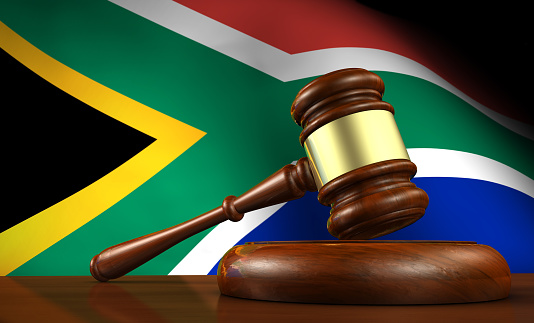 South Africa law and justice concept with a 3d render of a gavel on a wooden desktop and the South African flag on background.