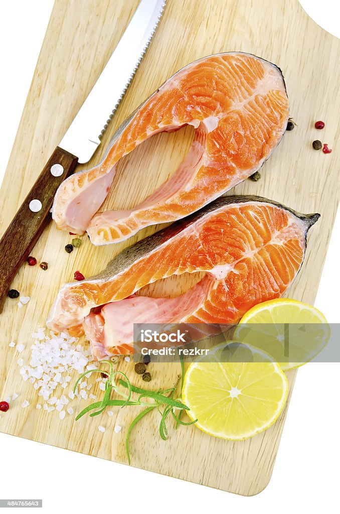 Trout with rosemary and knife on plank Two pieces of trout with rosemary, lemon and coarse salt, a knife on a wooden board isolated on white background Colors Stock Photo