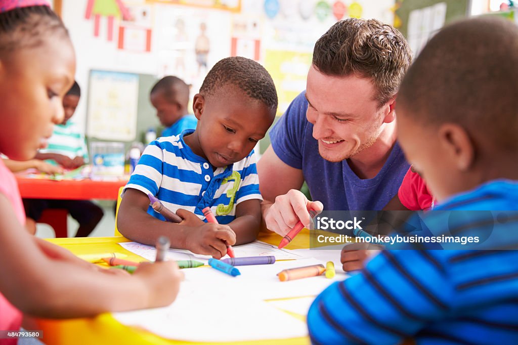 Volunteer teacher helping a class of preschool kids drawing Teacher Stock Photo