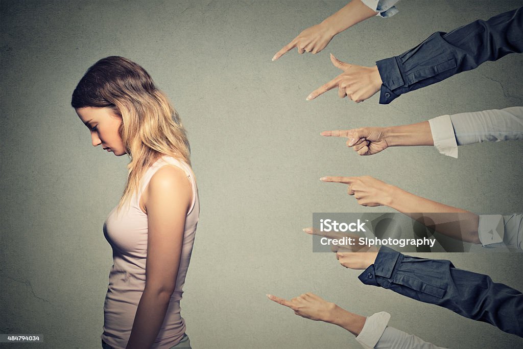 Concept of accusation guilty person girl Concept of accusation guilty person girl. Side profile sad upset woman looking down many fingers pointing at her back isolated on grey office wall background. Human face expression emotion feeling Judgement Stock Photo