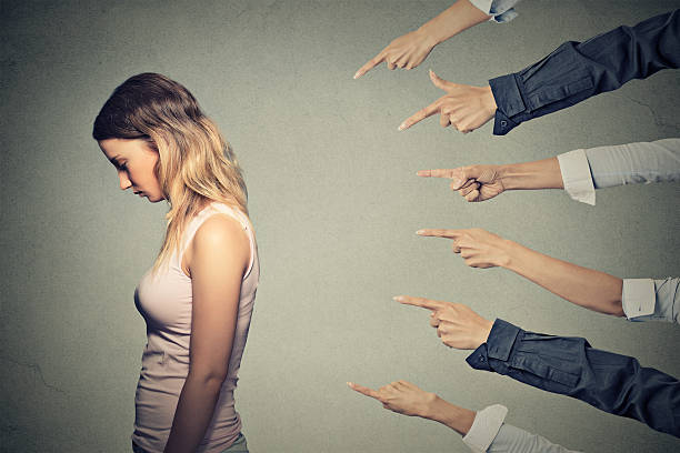 Concept of accusation guilty person girl Concept of accusation guilty person girl. Side profile sad upset woman looking down many fingers pointing at her back isolated on grey office wall background. Human face expression emotion feeling judgement photos stock pictures, royalty-free photos & images