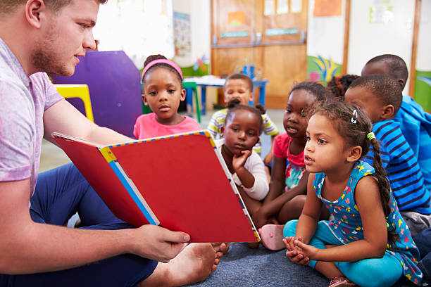 Volunteer teacher reading to a class of preschool kids Volunteer teacher reading to a class of preschool kids cross legged photos stock pictures, royalty-free photos & images