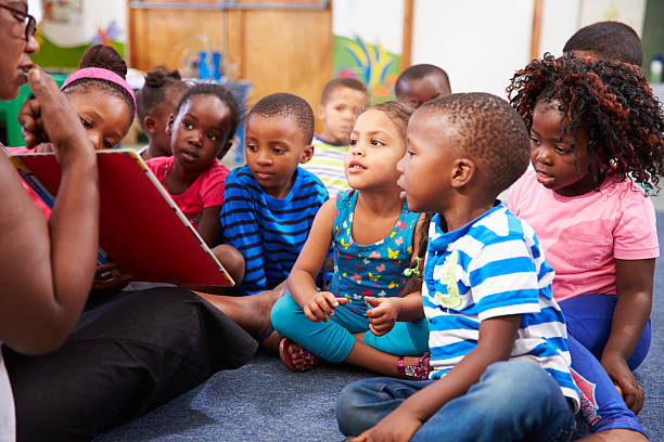 professor ler um livro com uma aula de crianças pequenas, crianças - africa child reading african descent - fotografias e filmes do acervo