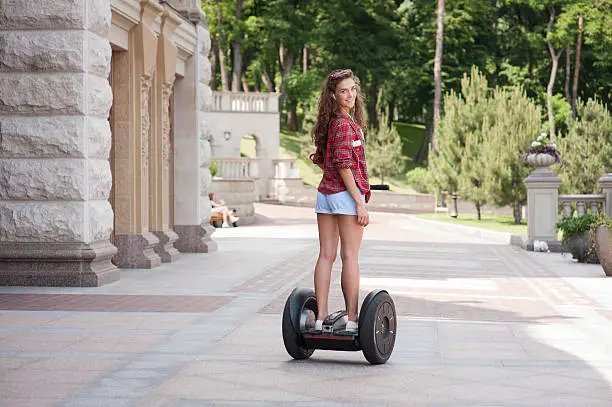 Back view photo of beautiful young woman. Girl using segway, listening to music and smiling