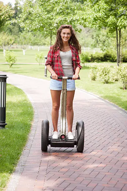 Portrait of beautiful young woman. Girl using segway, looking at camera and smiling. Green alley as background