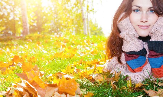 Woman with red hair laying on autumn leaves. She has gloves and a multicolored sweater.