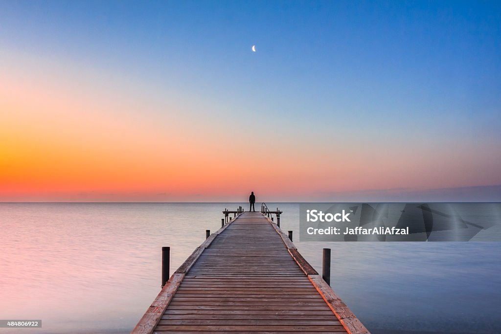 Mann, stehend auf Anlegesteg am Strand mit sunrise und Mond - Lizenzfrei Ende Stock-Foto