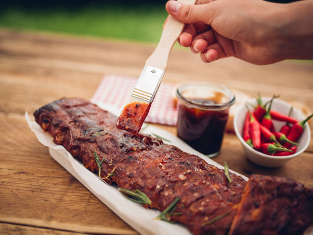 cepillo de pintura salsa de barbacoa en un rack de las costillas - marinated fotografías e imágenes de stock