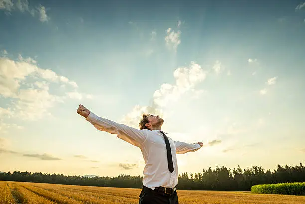 Half Body Shot of a Thankful Young Businessman Looking up the Sky with Wide Open Arms, Standing at the Open Field.