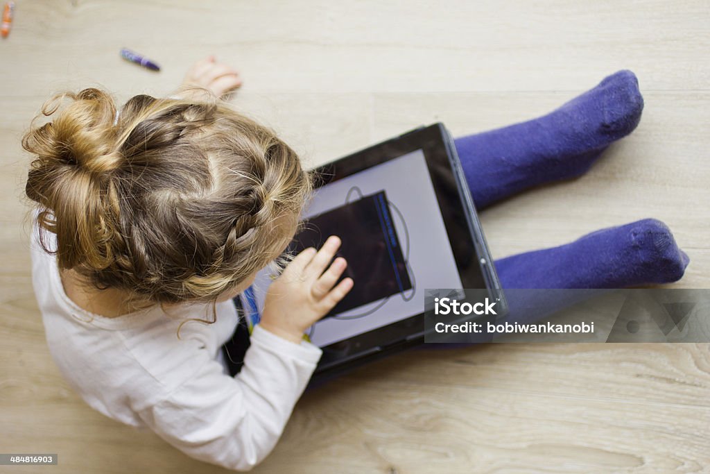 Little girl with a digital tablet Little girl using digital tablet on the parquet floor.Crayons are no longer in vogue... Girls Stock Photo