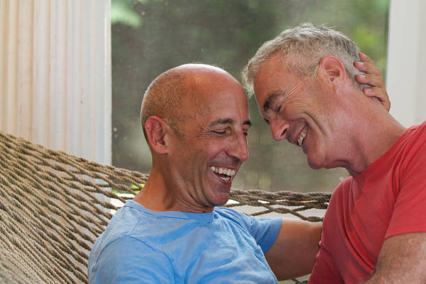 Senior gay men affectionate and smiling on vacation in hammock stock photo