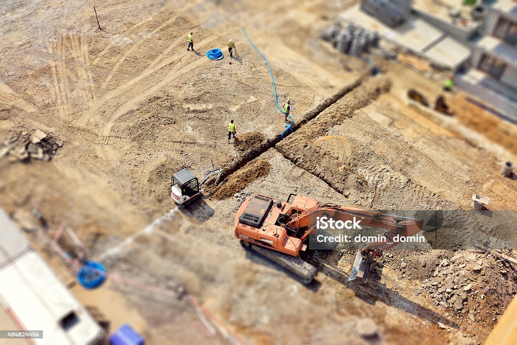 Workers, Engineers digging in ground, sewer system, street, tilt-shift, above Manual workers and Engineers are digging a raw in the ground, they do drainage, sewer system, then make a new asphalt road. Directly above, tilt-shift. Construction Site Stock Photo