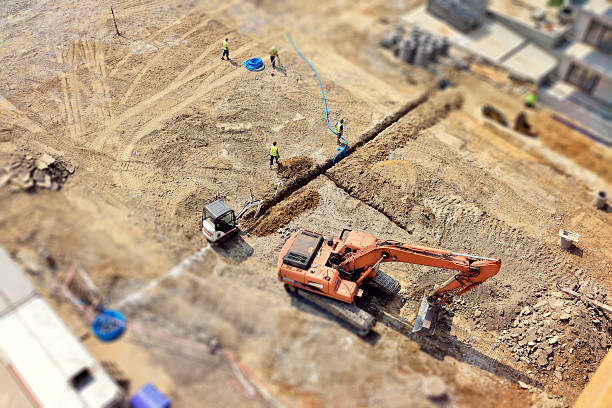 Workers, Engineers digging in ground, sewer system, street, tilt-shift, above Manual workers and Engineers are digging a raw in the ground, they do drainage, sewer system, then make a new asphalt road. Directly above, tilt-shift. tilt shift stock pictures, royalty-free photos & images