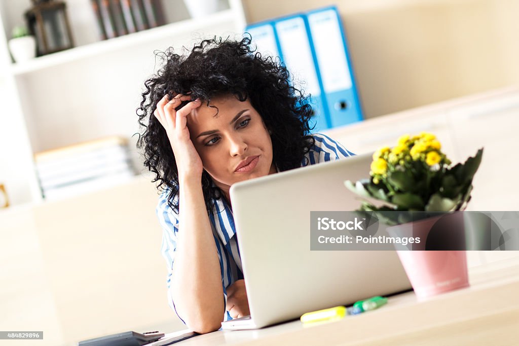 Exhausted Businesswoman looking at laptop Exhausted Businesswoman looking at laptop in her office 2015 Stock Photo