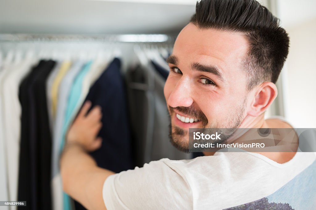 Smiling man choosing clothes Selecting wardrobe in a good boutique. Young content man choosing jacket. Closet Stock Photo