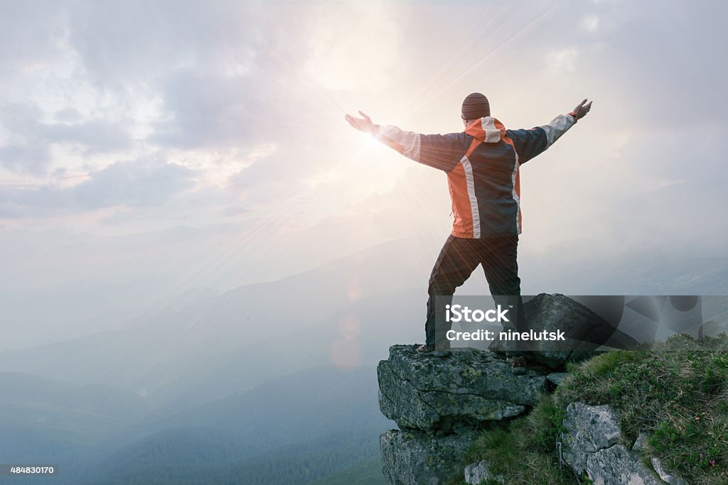 Man standing on the rock in the mountains Happy man standing on the cliff of mountain with raised hands to the sun.  Hiker celebrating success. 2015 Stock Photo