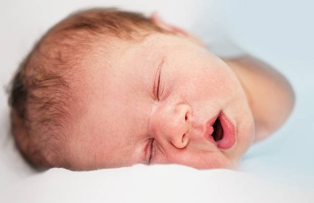 istock Headshot of Sleeping Newborn with open mouth on white bed 484840834