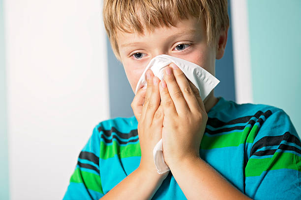 istock ill boy with flu blowing nose at home 484852636