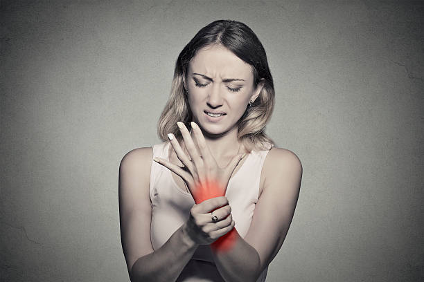 woman holding her painful wrist Young woman holding her painful wrist isolated on gray wall background. Sprain pain location indicated by red spot. Negative face expression . arthritis stock pictures, royalty-free photos & images