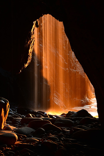 Natural long exposure from the bowels of the earth, with a setting Sunlight shining through a waterfall curtain.