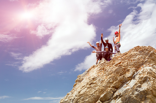 Happy people embracing raising hands up on pointed rocky cliff blue sky background