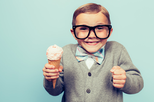A young nerd boy with glasses loves eating sugary treats such as ice cream cones. He is smiling broadly and is excited to eat junk food. Retro styled  